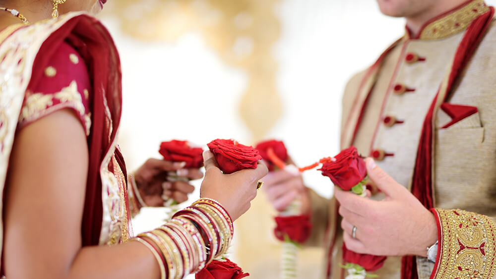 Indian married couple in traditional attire holding roses