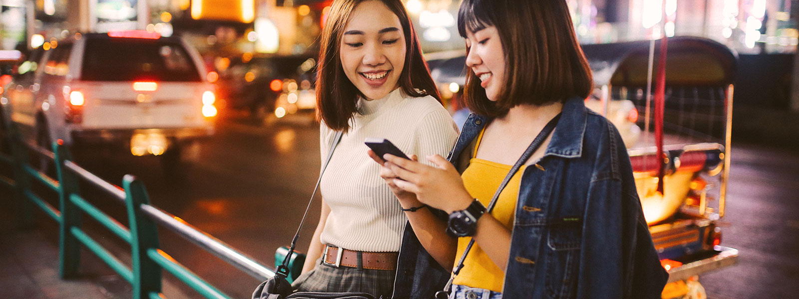 Two women looking at a phone on a street in Thailand