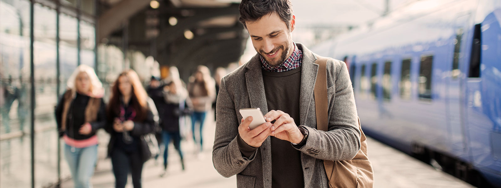 Man at a train platform smiling at his phone